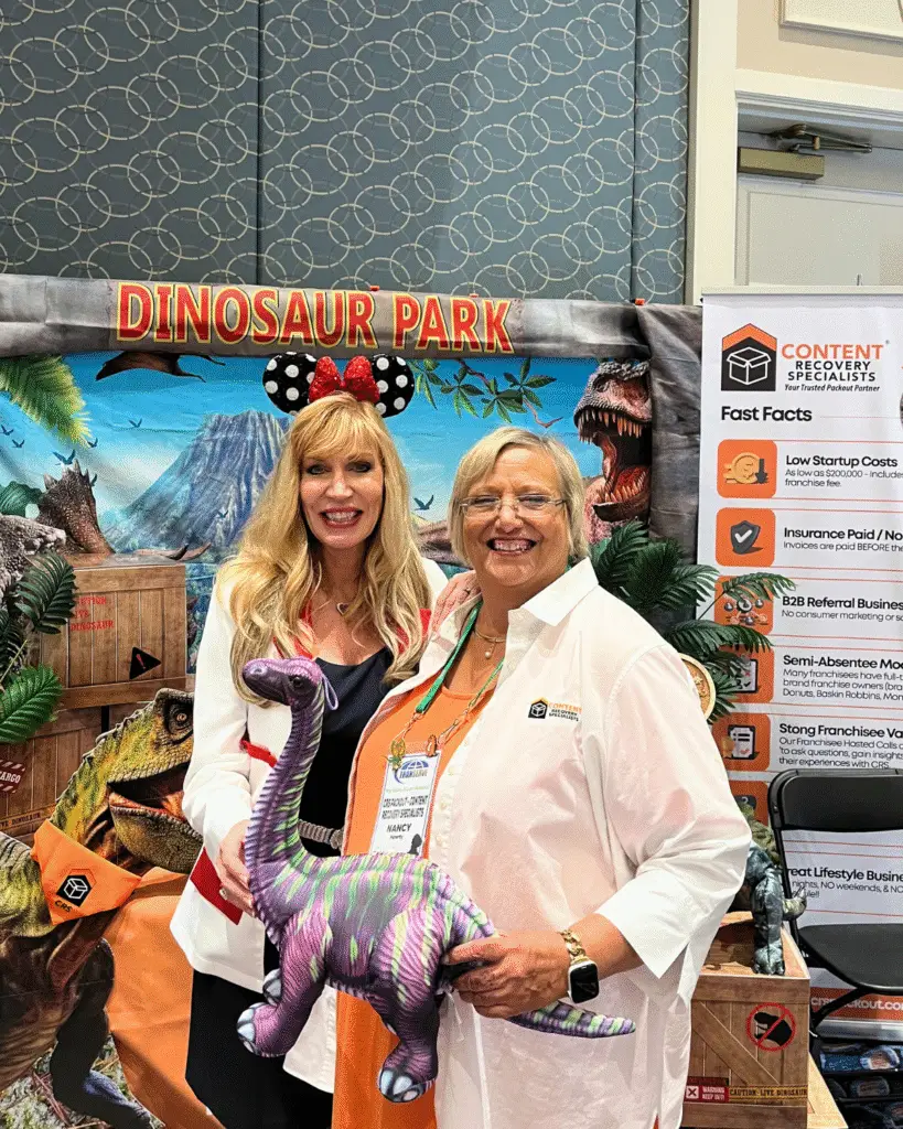 Nancy Haverty of CRS poses with CEO of Franserve, Alesia Visconti holding the Purple Dinosaur for the Best Dino Booth